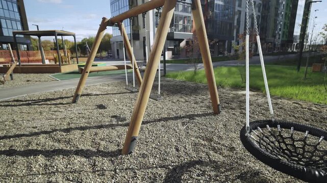 Net hammock and swings on empty sunny playground in apartment complex yard. Modern amusement children equipment installed in urban park