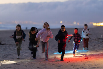 Children running on beach at dusk with colorful lights