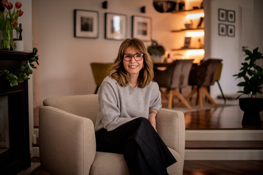 Blond haired middle aged woman relaxing in an armchair in her elegant home