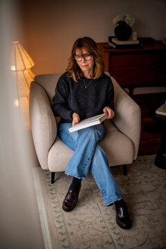 Blond haired woman in casual clothes with a book in her hand relaxing at home