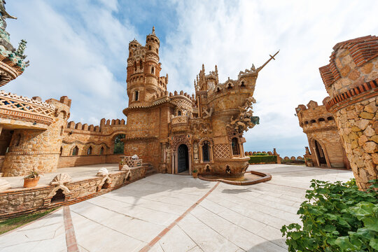 Castillo Monumento Colomares in Benalmadena shows towers, Mozarabic arches, sculpted prows, and carvings around an open portal as tourists explore under soft daylight.