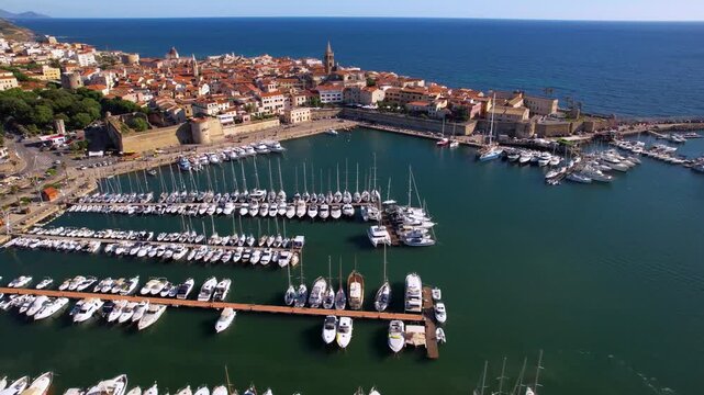 Alghero marina aerial flight to old town center with historic churches and cathedral reveal shot Sardinia Italy yachts in harbor Mediterranean coast drone footage 4k travel destination scenery