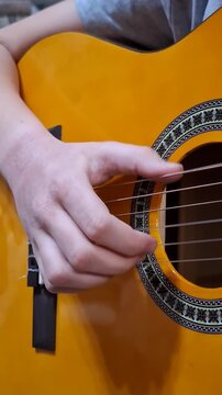 Detailed shot of a classic acoustic guitar featuring a bright yellow glossy finish and traditional circular patterns around the sound hole. A hand is captured in motion while plucking the strings
