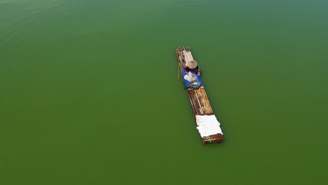 Fisherman casts net over calm on a bamboo raft, greenish water