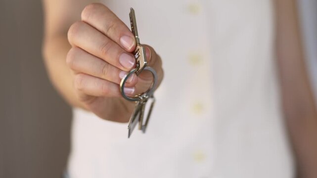 Close-up of real estate agent presenting house keys, with the keyring held prominently between the fingers, symbolizing an affordable home purchase, set against a bright and welcoming background