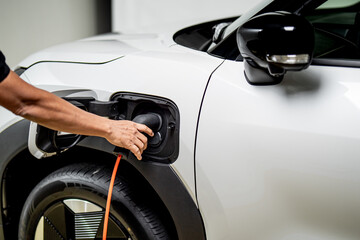 Naklejka premium Close up of person plugging charging cable into electric vehicle charging port on modern white EV car.