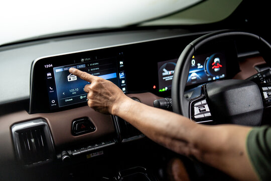 Driver touching infotainment touchscreen to select radio station inside modern vehicle dashboard, digital car entertainment system interface.
