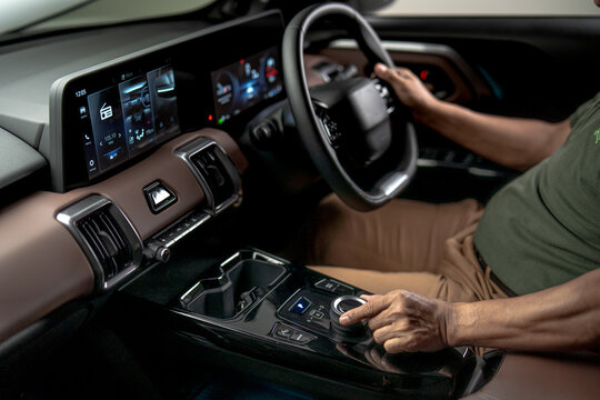 Driver adjusting rotary controller on center console while driving modern vehicle with digital dashboard and infotainment display.
