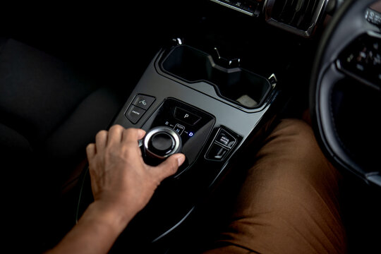 Driver operating rotary gear selector on center console of modern electric vehicle interior.
