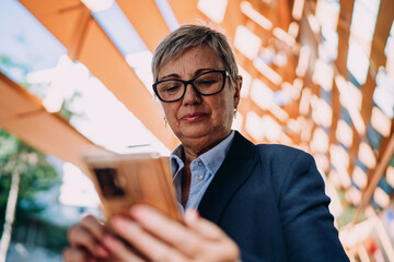 Close-up of mature woman looking at smartphone outdoors, expressing concentration and digital...