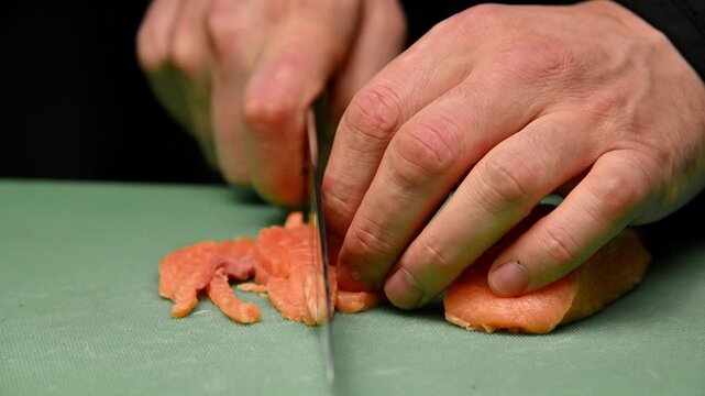 Chef slices salmon fillets into smaller pieces on green cutting board