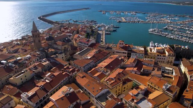 4K Aerial View of Alghero Old Town and Marina. Cinematic Drone Flight over Red Roofs, Historic Churches and Bastions towards Port with White Sailing Boats. Sardinia Italy. High Quality Video