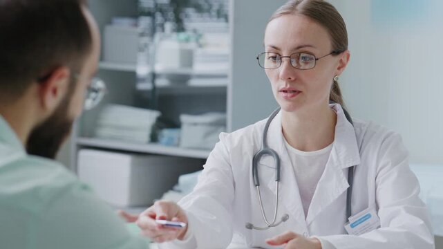 Female doctor giving medical consent form to patient and explaining where to sign it during consultation at clinic. Tilt up shot