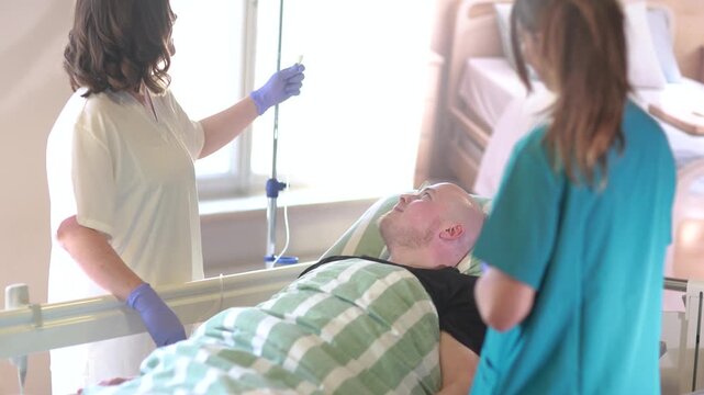 Senior nurse demonstrates IV infusion management to nursing student while caring for young male patient in hospital bed