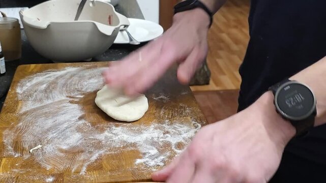 Baker shaping and rolling dough on wooden board. Man cooking in kitchen to prepare pastry. Manual culinary technique with flour for homemade food production process.