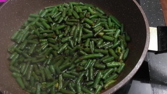 Green bean cuts saut&eacute;ing in a metal pan. Vegetarian food preparation process in home kitchen. Healthy vegetable meal cooking concept for nutritious dinner menu.