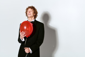 Obraz premium Elegant young man in a tuxedo celebrates with a balloon in a joyful studio setting