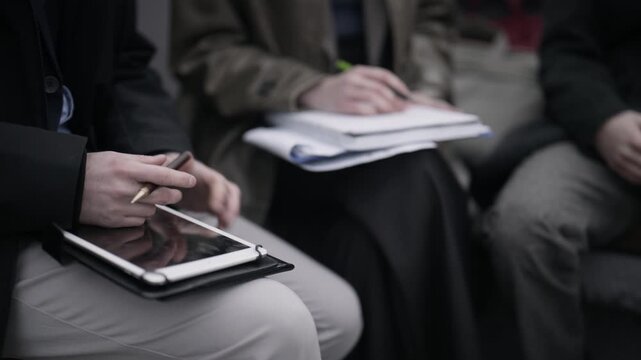 Young business associates are seen engaging in a collaborative session. They are utilizing digital tablets and notepads to exchange ideas and information.