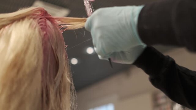 Hairdresser in blue gloves applying pink dye to a blonde mannequin head during a styling session