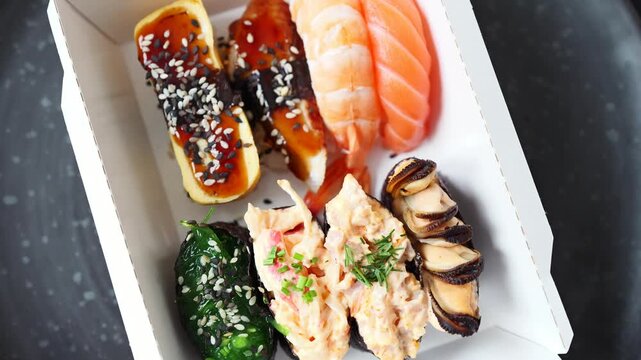 Delicious Japanese sushi meal packed in a transparent container. Features salmon, eel, and crab topped rolls, ready for delivery.