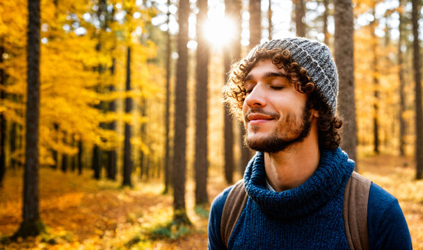 smiling young man with curly hair and beanie enjoying autumn sun in a yellow forest