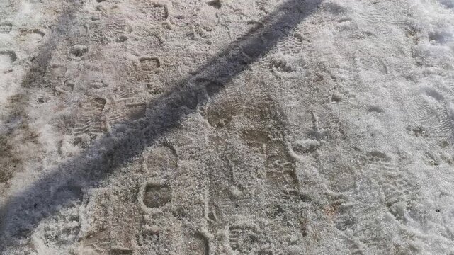 Footprints and handprints visible in snow-covered ground, showing a progression of movement across the surface with shadows cast by nearby objects