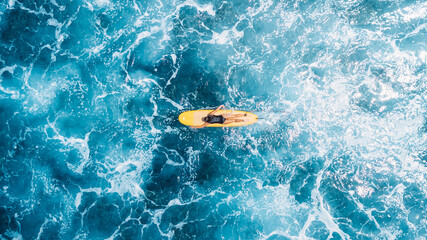 Fototapeta premium Woman on surfboard in blue ocean. Drone view of surfer during surfing