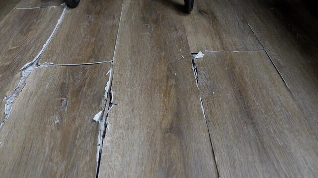 buckled laminate floor with torn planks and visible crack caused by heated floor expansion. closeup of damaged floor covering with lifted edges