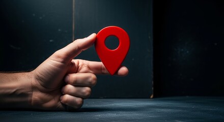 Fototapeta premium Male hand holding a bright red three dimensional map location pin icon against a dark background