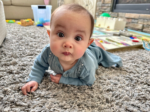 Close-up of a baby girl in a babygro lying on a rug surrounded by toys in a living room