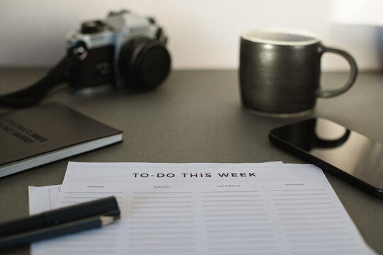 Close-up of a To do list, notebook, pens, mobile phone, camera and a cup of black coffee on a desk