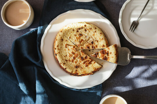 Close-up overhead view of a slice of Basque Burnt Cheesecake being served and two cappuccinos on a table