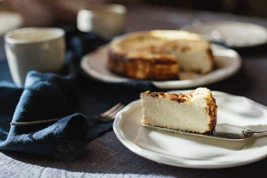 Close-up of a slice of Basque Burnt Cheesecake on a table with cups of coffee for afternoon tea