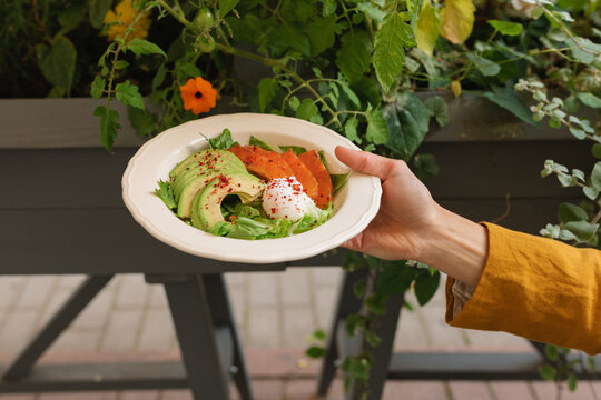 Close-up of a woman standing in a garden in summer holding a bowl with a salmon, avocado, and poached egg salad