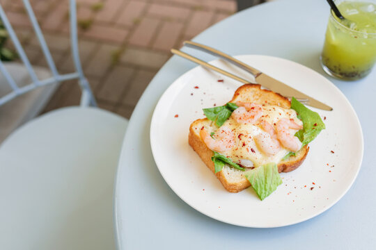 Close-up of a shrimp toast with a poached egg and greens on an outdoor garden table with a refreshing passion fruit and chia drink