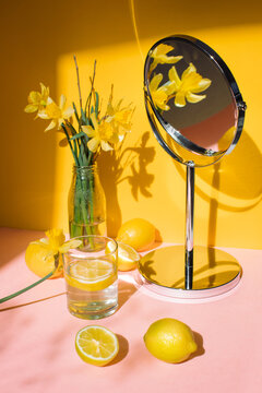 Bunch of yellow daffodils on a table reflected in a mirror with fresh lemons and a glass of lemon water on a table