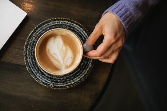 Overhead view of a woman's hand reaching for a cappuccino on a wooden table