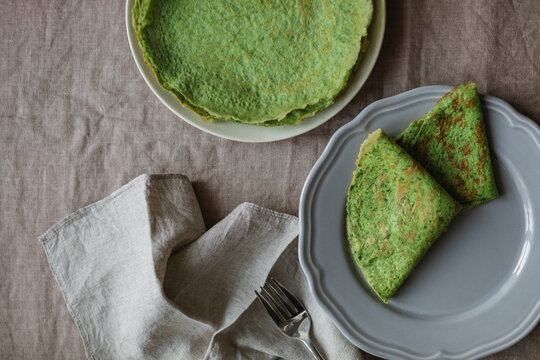 Overhead view of a stack of homemade gluten free spinach pancakes, two pancakes on a plate on a linen tablecloth with a napkin