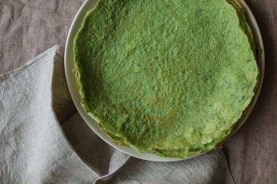 Overhead view of a stack of homemade gluten free spinach pancakes on a plate on a linen tablecloth with a napkin