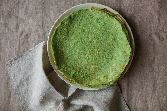 Overhead view of a stack of homemade gluten free spinach pancakes on a plate on a linen tablecloth with a napkin