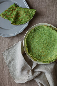 Overhead view of a stack of homemade gluten free spinach pancakes and two pancakes on a plate on a linen tablecloth with a napkin