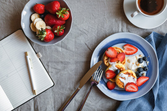 Overhead view of homemade keto cottage cheese pancakes with fresh strawberries and blueberries, a bowl of strawberries and a cup of tea on a table