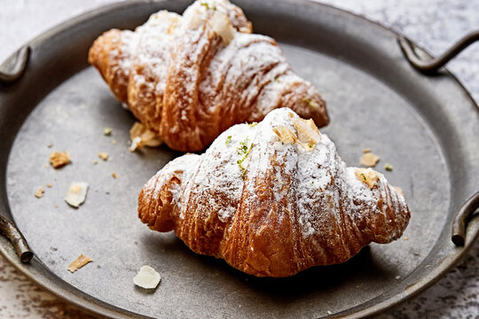Close-up of two croissants dusted with icing sugar on a metal tray