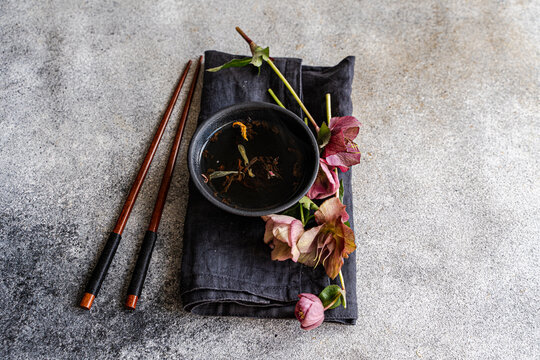Overhead view of a cup of herbal tea on a folded napkin with chopsticks and purple hellebore (Helleborus orientalis) flowers