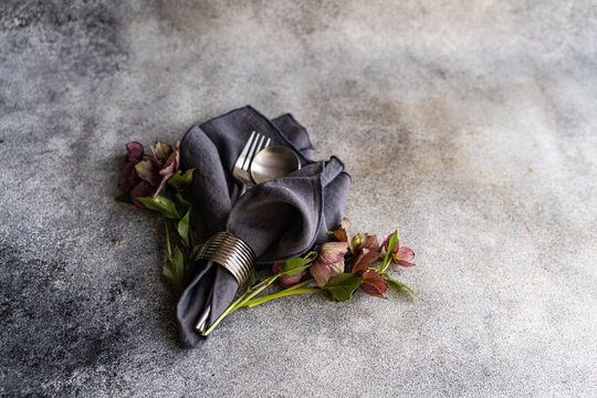 Overhead view of a springtime cutlery setting with fresh purple hellebore (Helleborus orientalis) flowers on a grey background