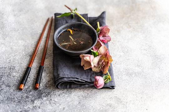 Overhead view of a cup of herbal tea on a folded napkin with chopsticks and purple hellebore (Helleborus orientalis) flowers