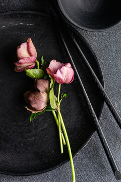 Close-up of an Asian table setting with black crockery, chopsticks and fresh purple hellebore flowers