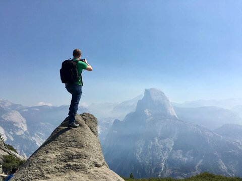 Rear view of a Male hiker standing on a rocky overlook taking a photo, Half Dome, Yosemite National Park, California, USA