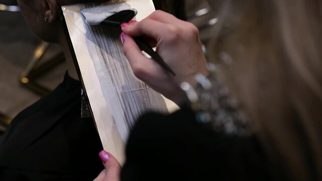 Professional hair stylist applying bleach to a section of blonde hair using a brush and foil