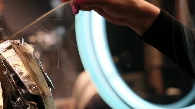 Professional hairstylist sections blonde hair for highlighting using aluminum foil and salon clips under ring lighting